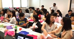 Over twenty people sitting at tables with baby dolls