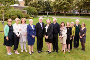 nine women and three men standing on the grass