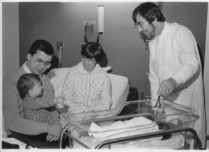 A doctor, man and woman introducing toddler to newborn baby